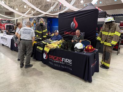 Firefighters talking at a booth displaying turnout gear, helmets and gloves at the 2026 WV Fire Expo