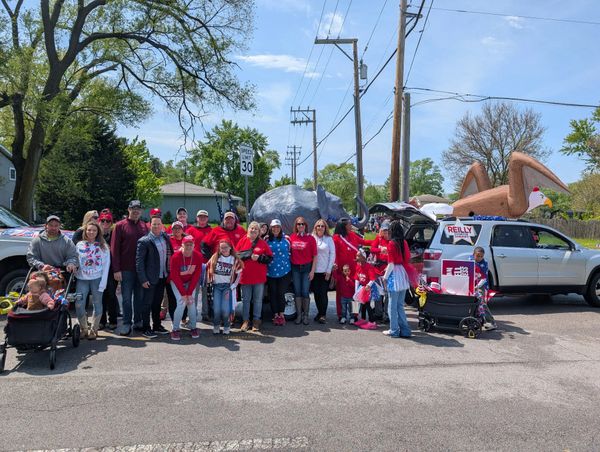 Group of people in red shirts posing on a street with decorated vehicles.