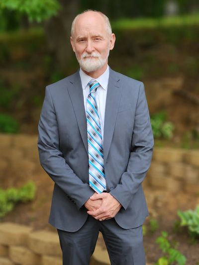 Elderly man in a suit standing outdoors with a confident smile.