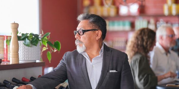 A man in a suit looks out a window in a warmly lit restaurant.