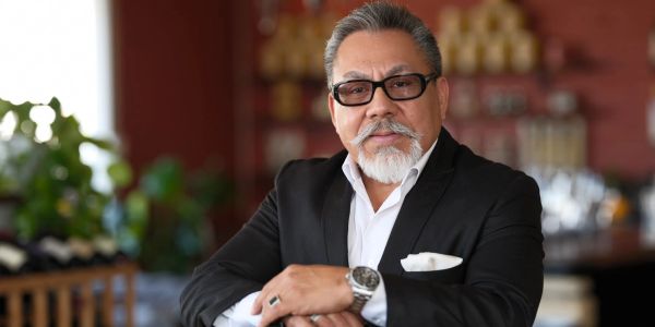 Confident older man in a black suit with glasses and a white beard.