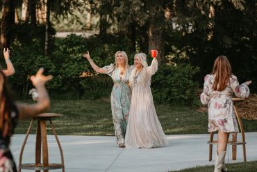 Two women happily pose outdoors with drinks.