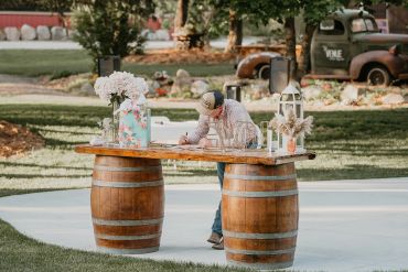 Person writing at a rustic outdoor table made from barrels.