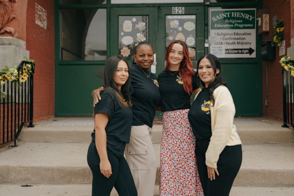 Four women posing happily outside a building with green doors.