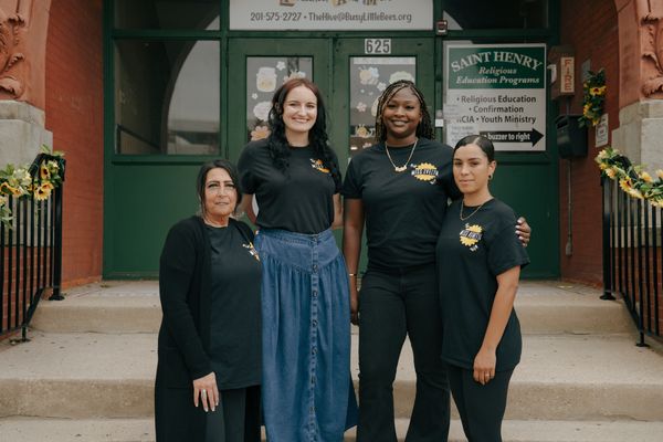 Four women in matching black shirts posing outside a building.