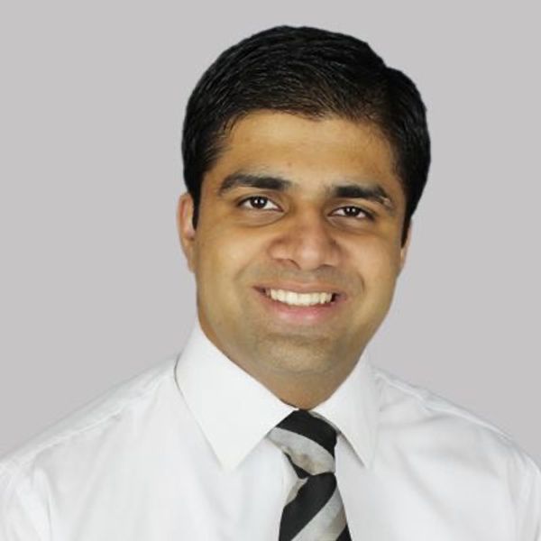 Smiling man in white shirt and striped tie against gray background.