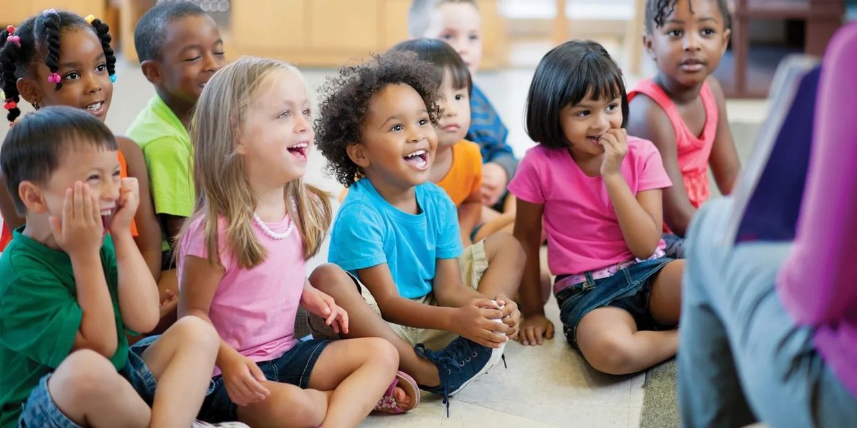 group of kids sitting down on the floor listening to someone reading a story