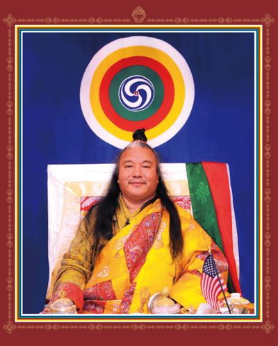 A man in traditional attire seated with a colorful circular symbol behind him.