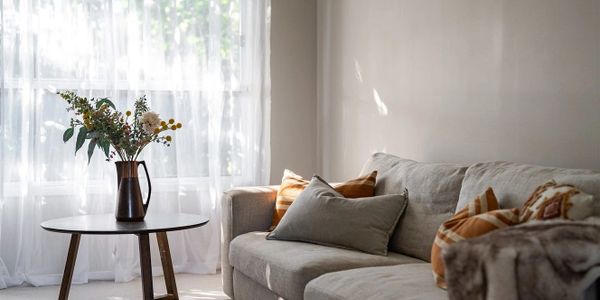 Cozy living room with soft natural light, a gray sofa, and a vase of flowers on a round wooden table.