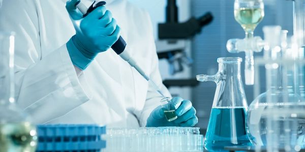 Scientist using pipette in lab with blue liquid.