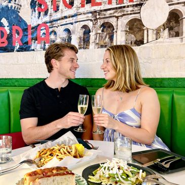 Couple smiling and toasting with champagne at a cozy restaurant.