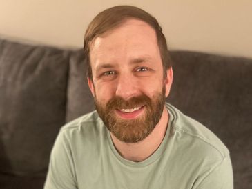 Smiling man with beard sitting on a couch.