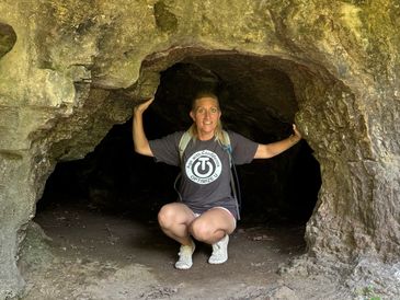 Woman crouching inside a small rocky cave opening.