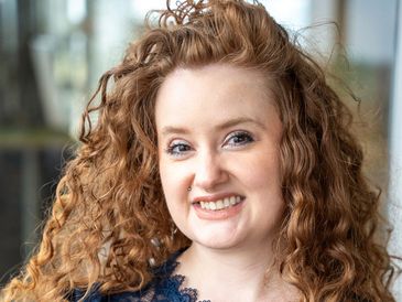 Smiling woman with curly red hair and a nose piercing.