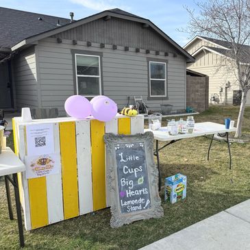 A lemonade stand with balloons and a chalkboard sign in front of a house.