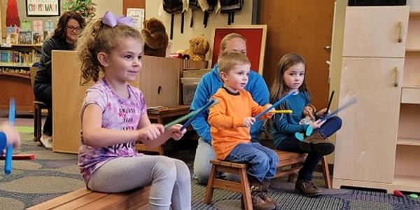 Picture of three kids with musical sticks sitting on brown benches.