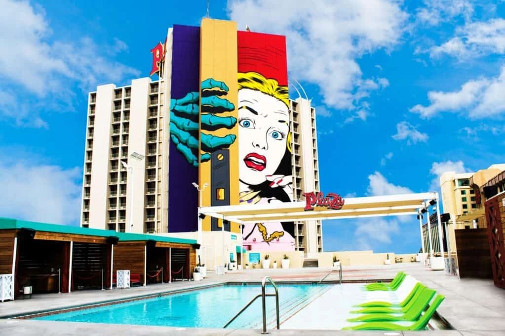 Colorful building mural behind a swimming pool with green lounge chairs.