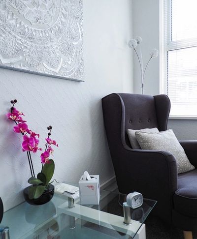 Cozy corner with a dark armchair, glass table, and vibrant pink orchids.