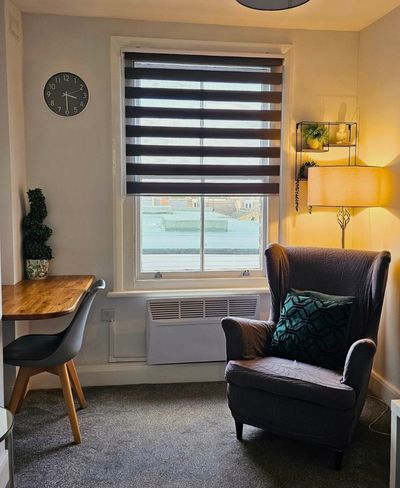 Cozy living space with armchair, desk, and window blinds.