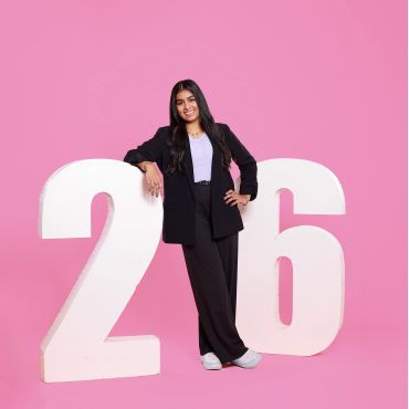Woman posing with large numbers 2 and 6 on pink background.