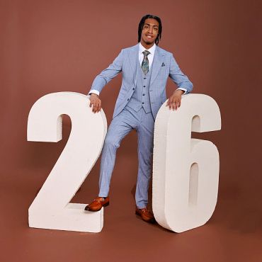 Young man in suit posing with large numbers 2 and 6.