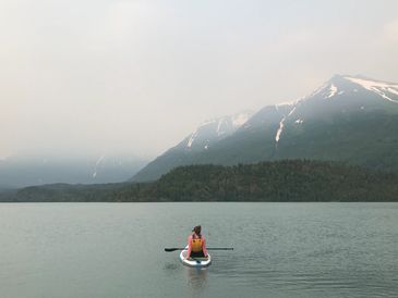 Person paddleboarding on a calm lake with snowy mountains in the background.