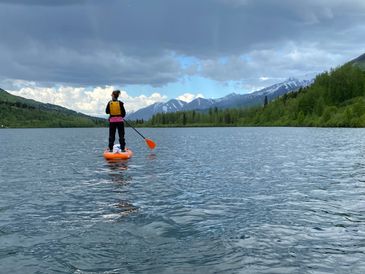 Two people paddleboarding on a lake with mountains in the background.