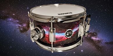 A snare drum with a galaxy-themed design against a starry background.