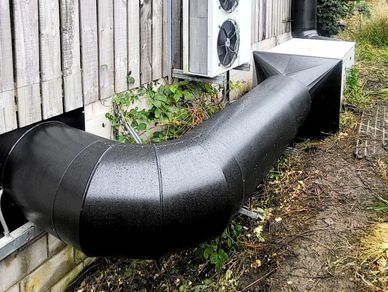 Large black ventilation ducts connected to a wooden building with an air conditioning unit.