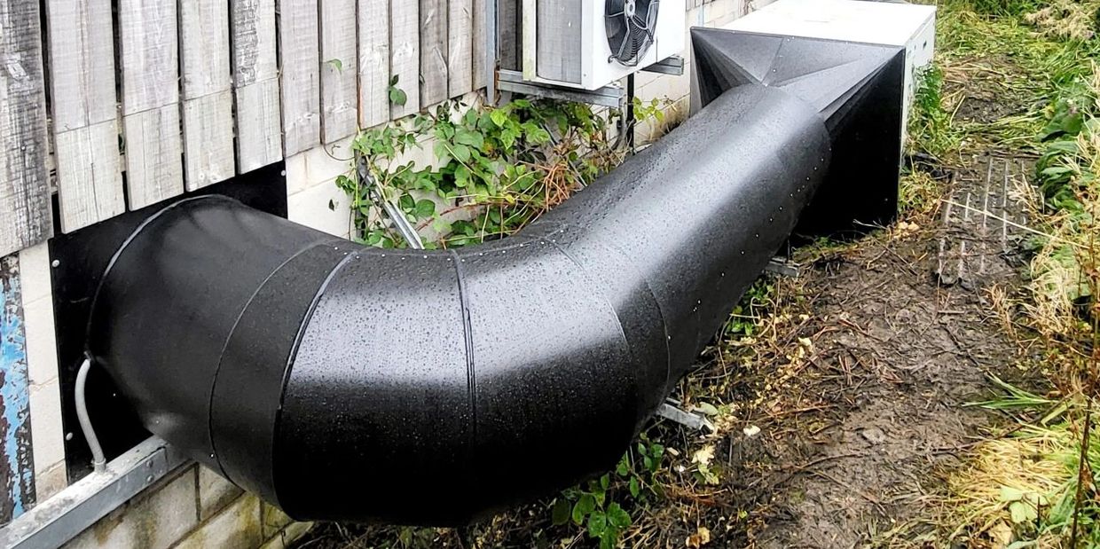Large black ventilation ducts connected to a wooden building with an air conditioning unit.