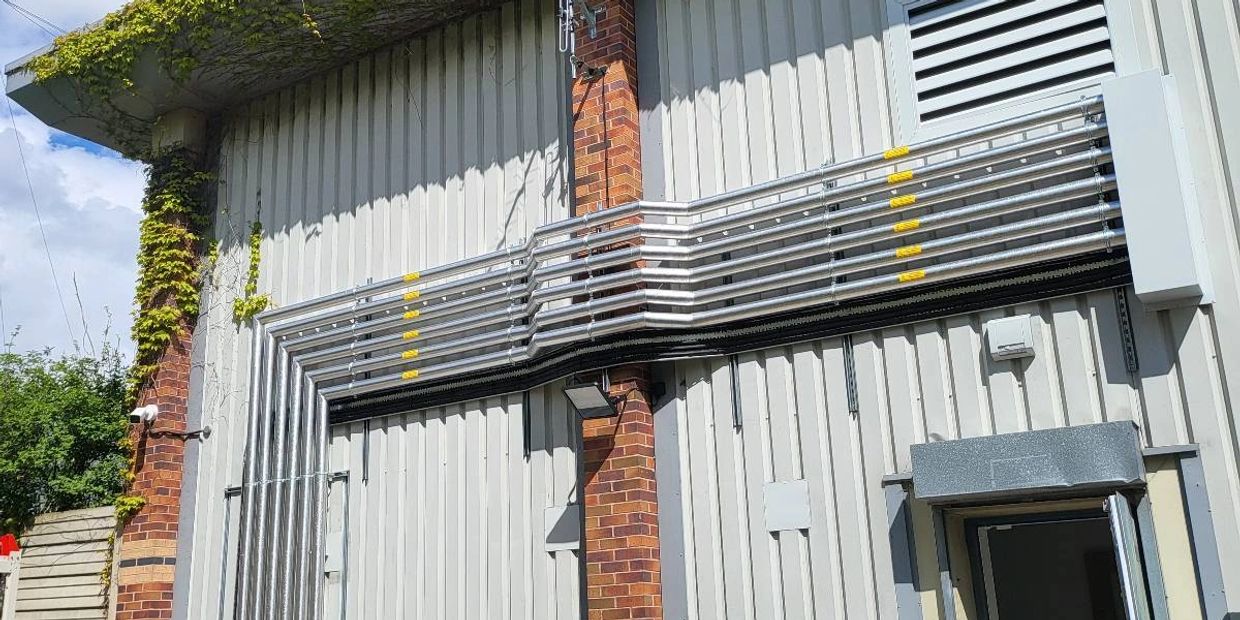 Industrial building exterior with pipes, air conditioning unit, and trash bins under a blue sky.