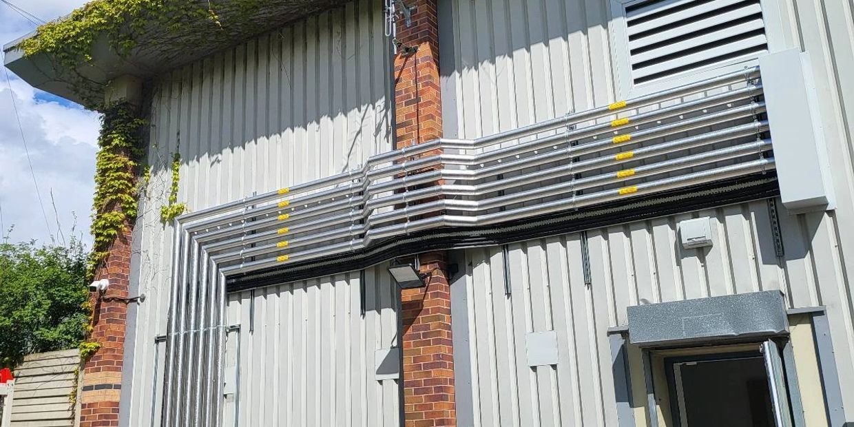 Industrial building exterior with pipes, air conditioning unit, and trash bins under a blue sky.