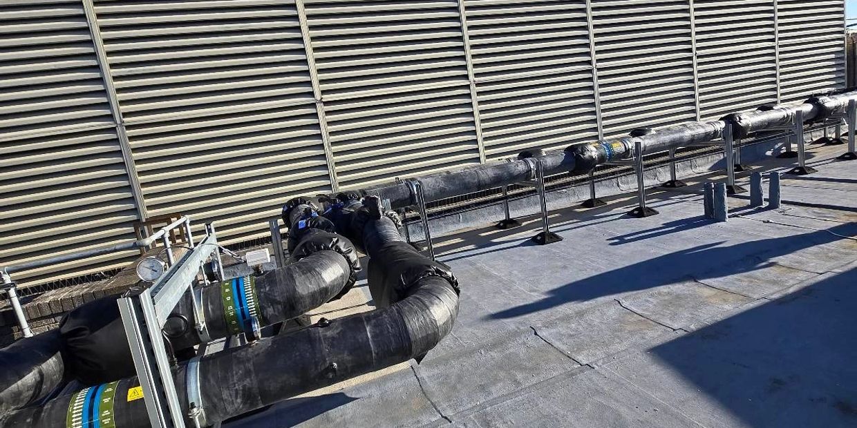 Industrial rooftop with insulated pipes under a clear blue sky.
