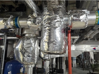 Insulated industrial pipes and valves in a mechanical room.