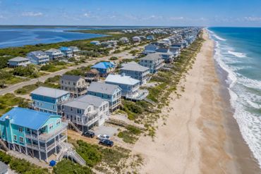Aerial view of coastal homes along a sandy beach under a clear blue sky.