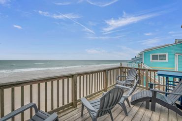 Beachfront deck with chairs overlooking the ocean and sandy shore.