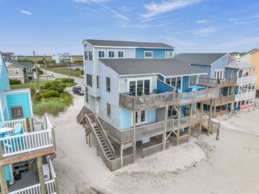 A three-story beach house with balconies facing the ocean under a blue sky.