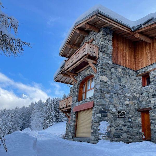 Stone and wood chalet in snowy mountain landscape under a clear blue sky.