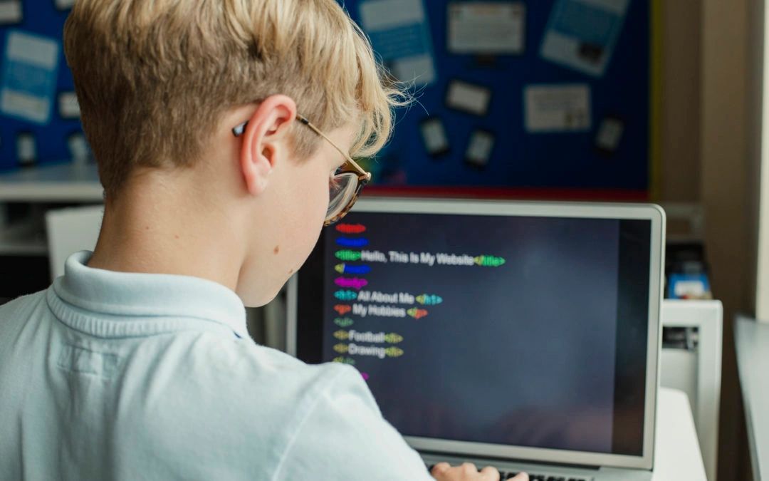 A young boy coding a personal website on a laptop in a classroom.