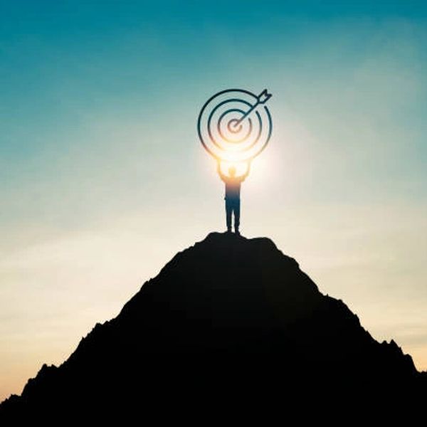 Person on mountain peak holding a glowing target symbol against the sky.