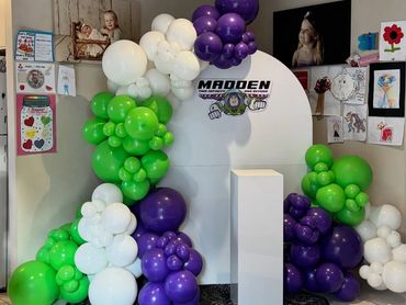 Colorful balloon arch in green, purple, and white with Madden logo backdrop for a celebration.