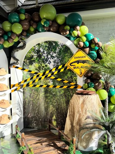 Jungle-themed party entrance with balloons and caution tape.