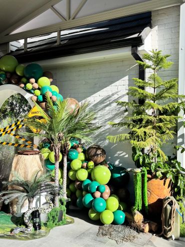 Jungle-themed party setup with green balloons and tropical plants.