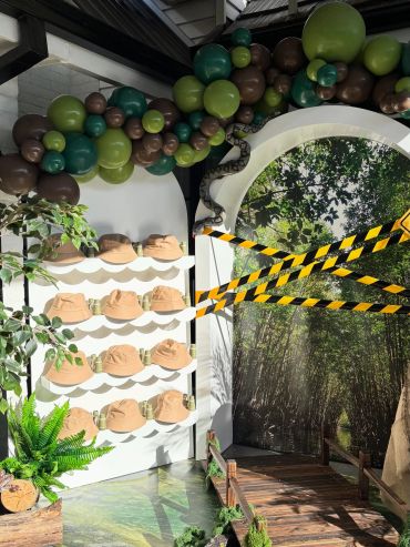 Jungle-themed display with hats, balloon arch, and caution tape.