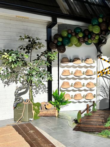 Decorative display with hats, green balloons, and a faux tree in a stylish indoor setting.
