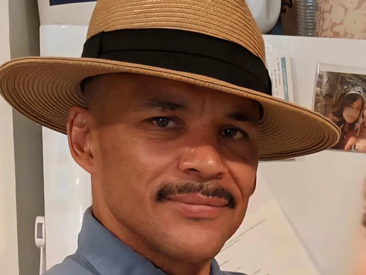 Man wearing a tan hat and blue shirt, smiling gently.