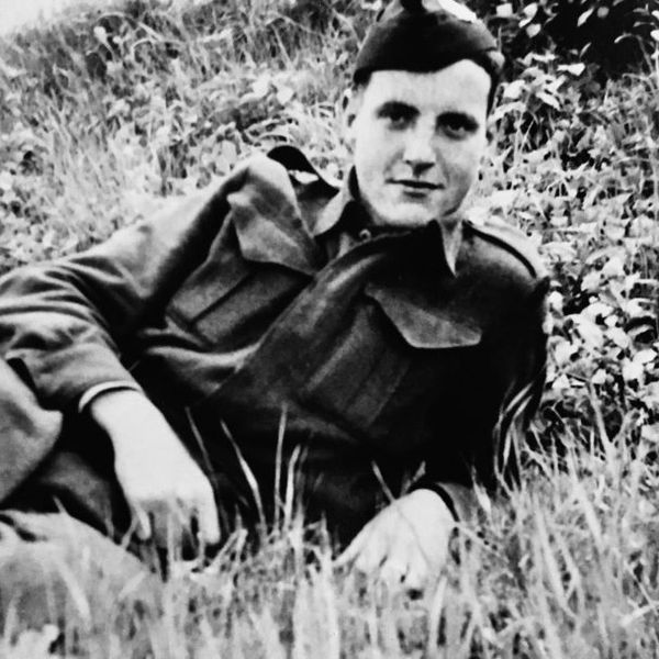 Black and white photo of a soldier lying in the grass, dressed in uniform.
