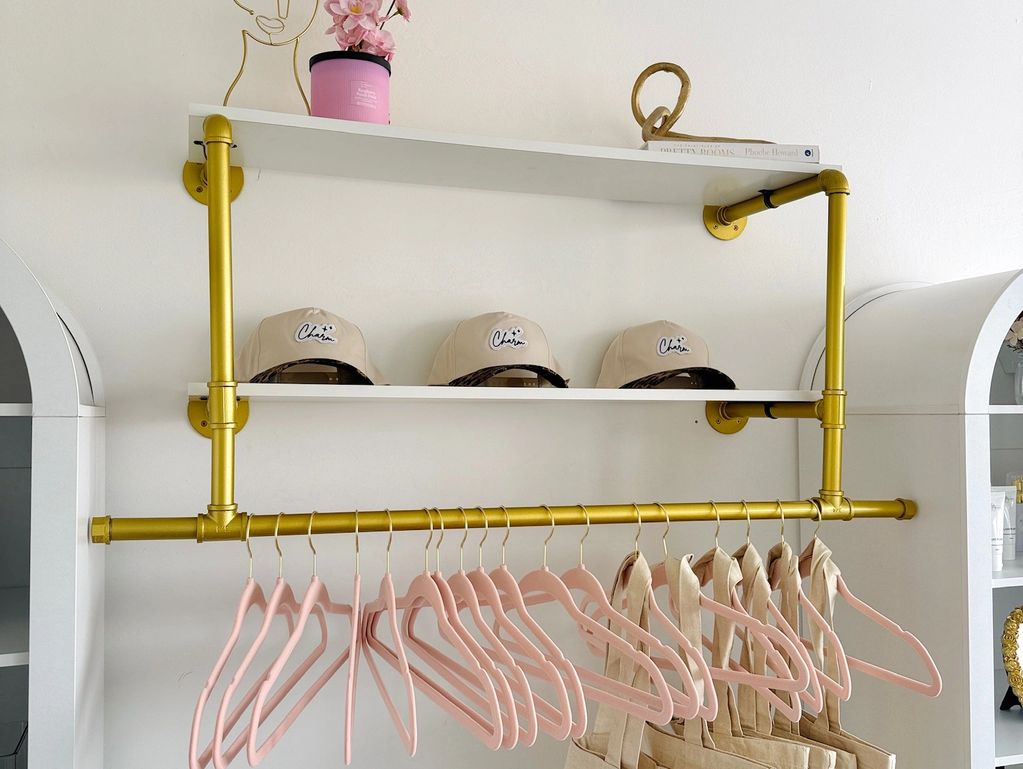Stylish gold rack with caps, pink hangers, and beige clothing in a minimalistic room.