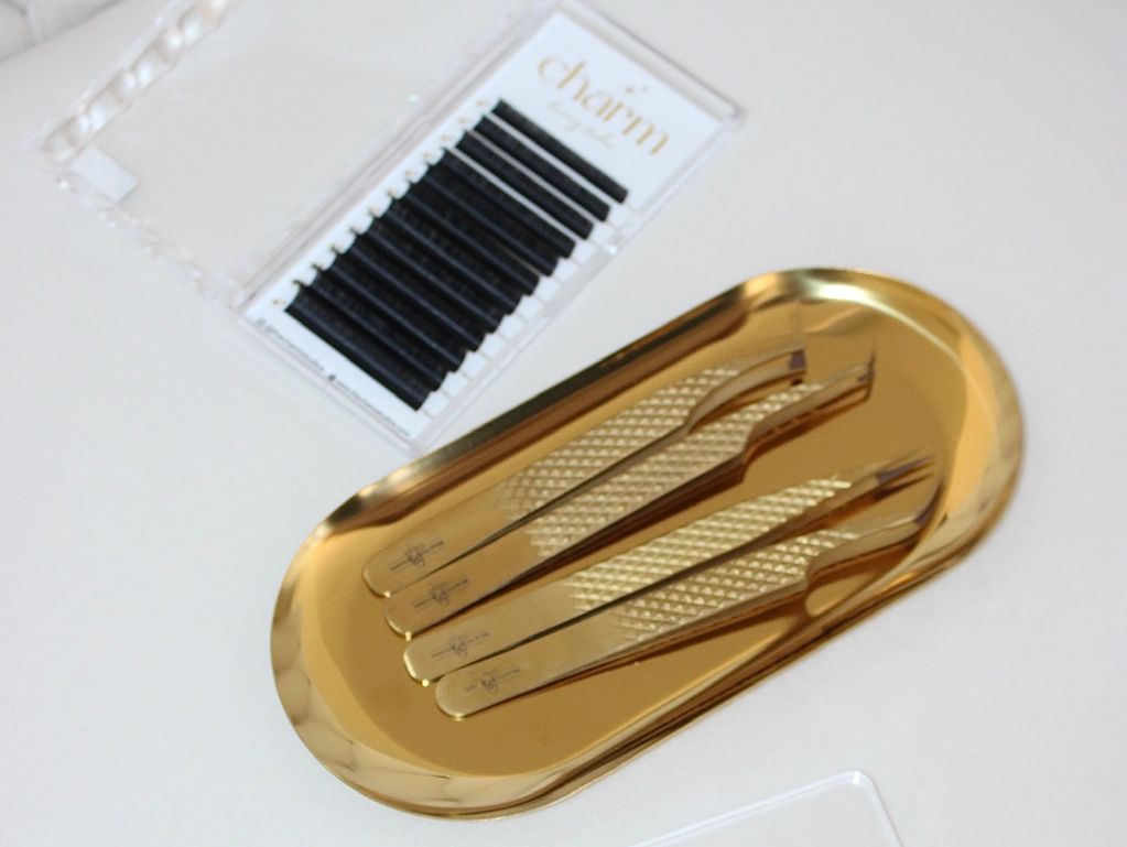 Gold tweezers on a golden tray with eyelash extensions nearby.