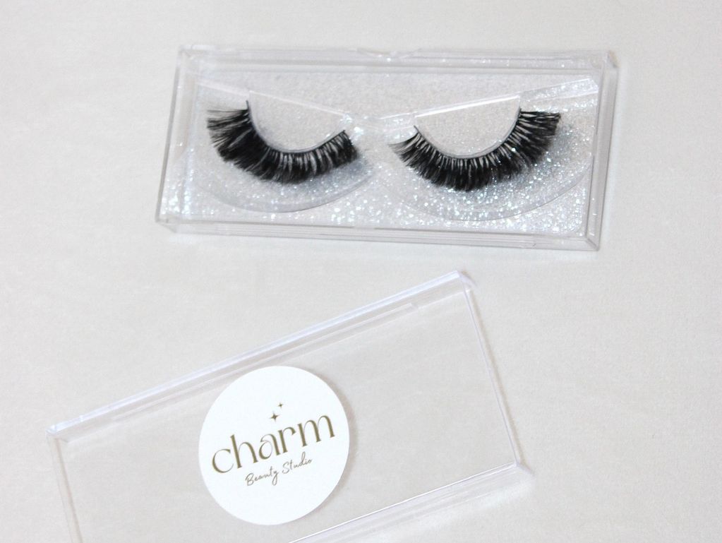 False eyelashes in a clear plastic case with Charm Beauty Studio branding.